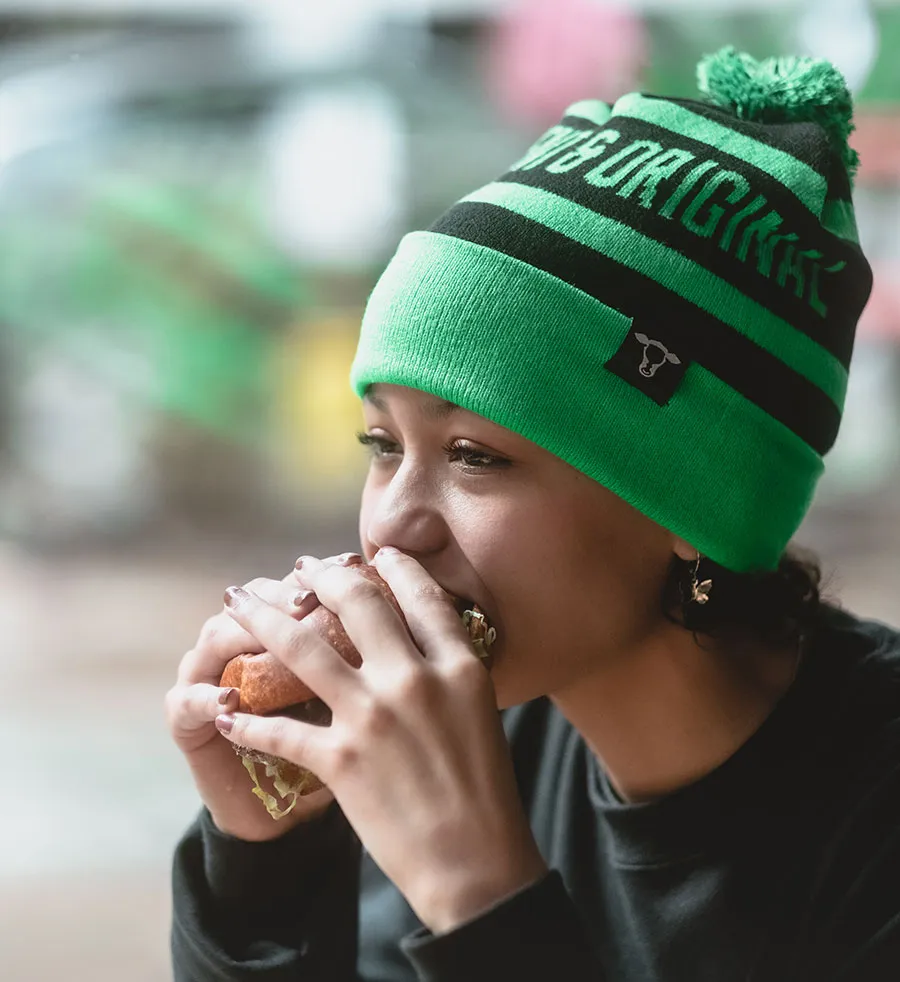 Woman wearing Hopdoddy ski hat and taking a bite out of a burger
