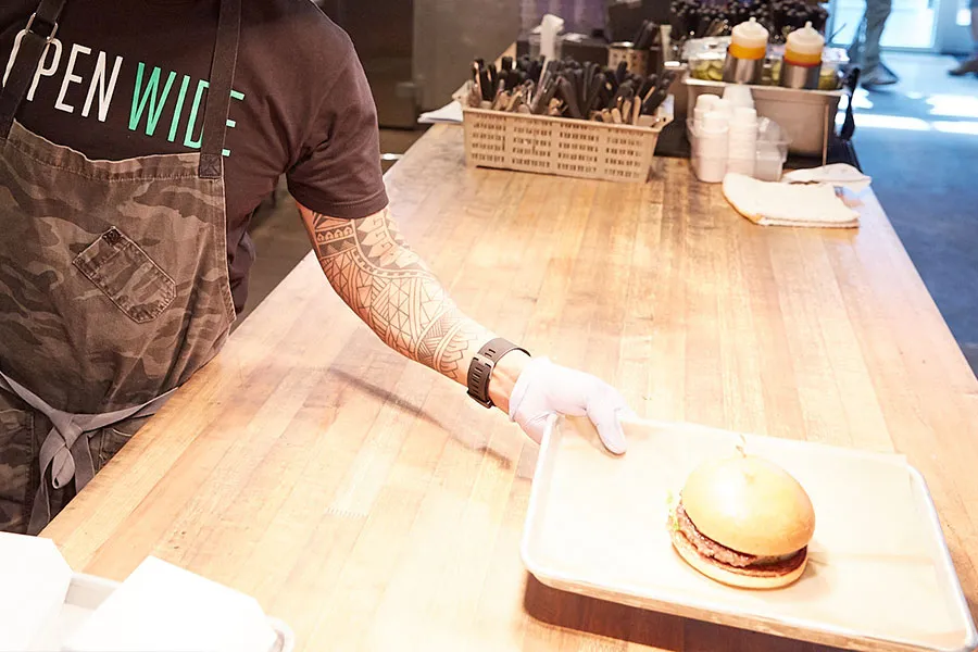 Long wooden counter with an employee serving up a burger