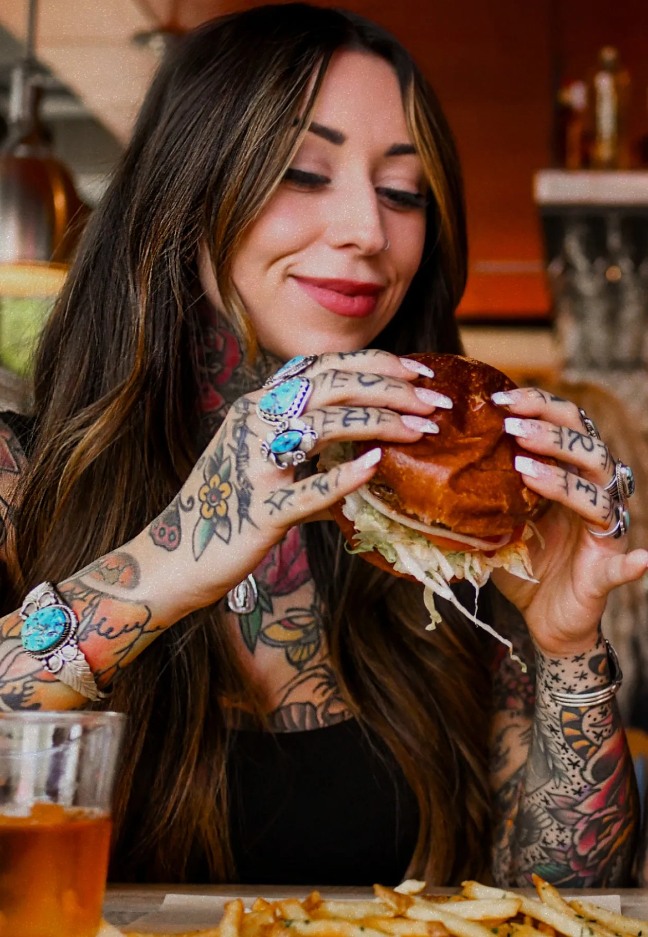 Woman holding a burger while looking at it with a soft smile on her face